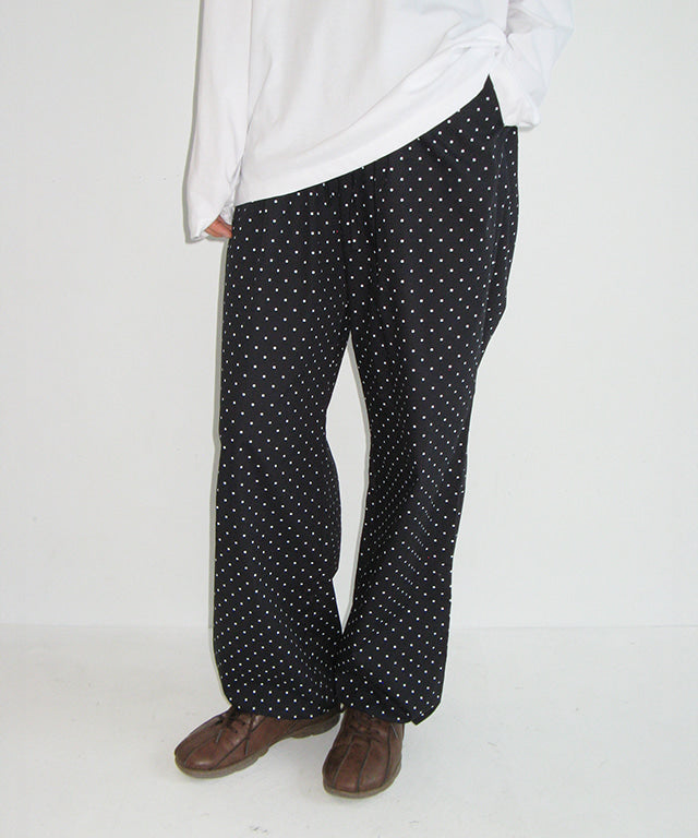 Person wearing black polka dot pants and a white top on a white background
