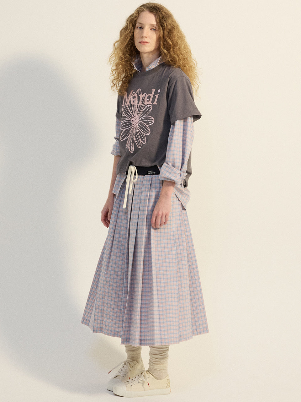 Person wearing a gray sweatshirt with a floral design and a plaid skirt on a light background