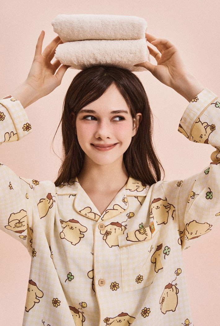 Woman wearing a pajama set with cartoon characters, holding folded towels above her head against a pink background.