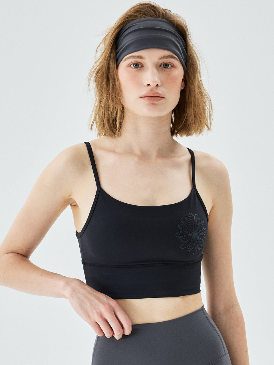 Woman wearing a black sports bra with a gray headband on a white background
