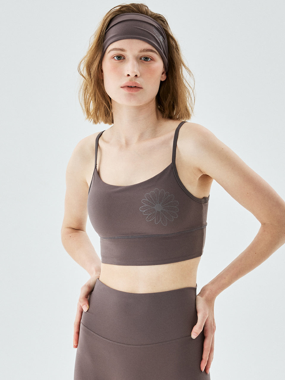 Woman wearing a brown sports bra and leggings with a white background