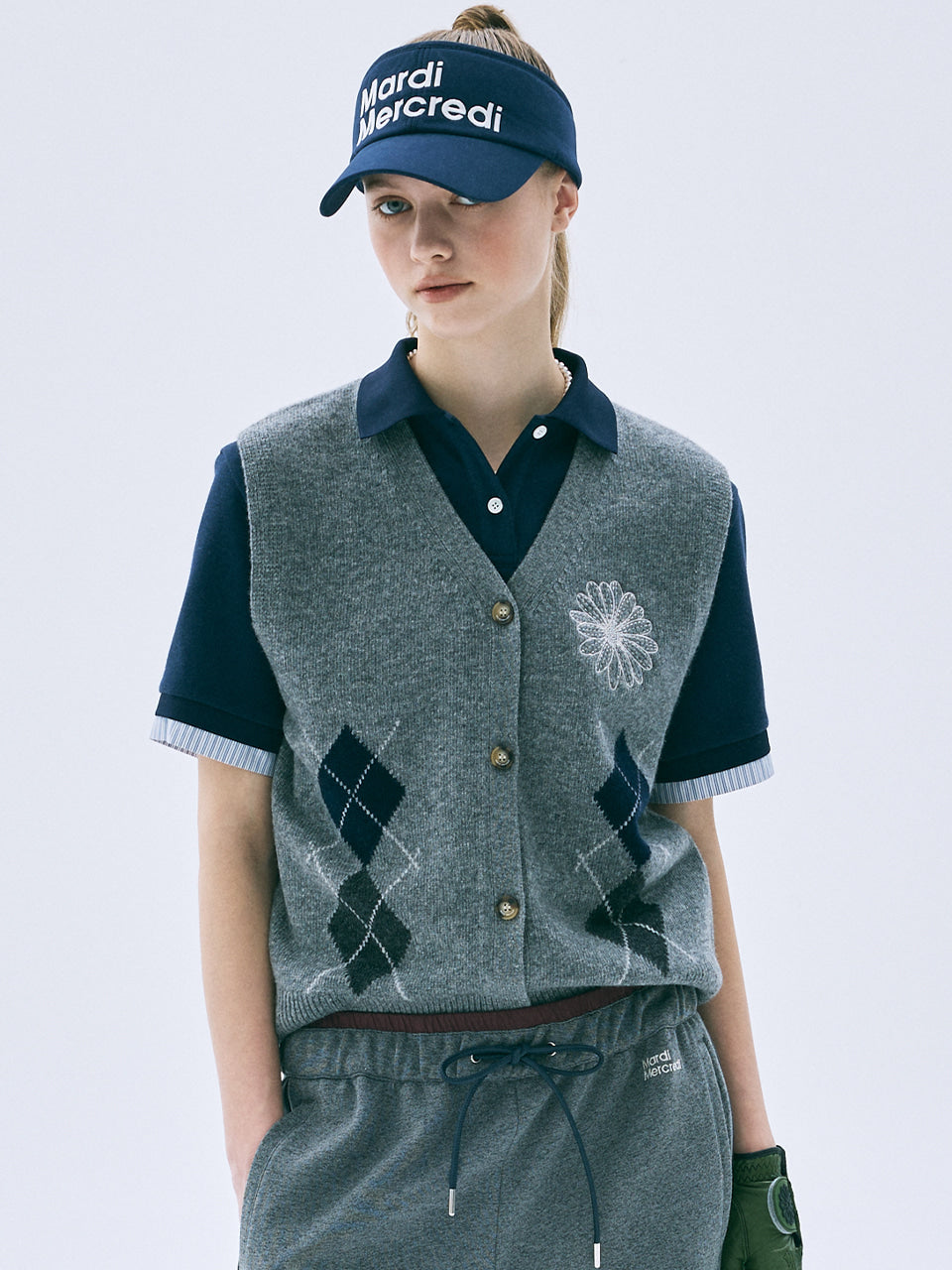 Person wearing a gray argyle vest over a navy shirt with a white background