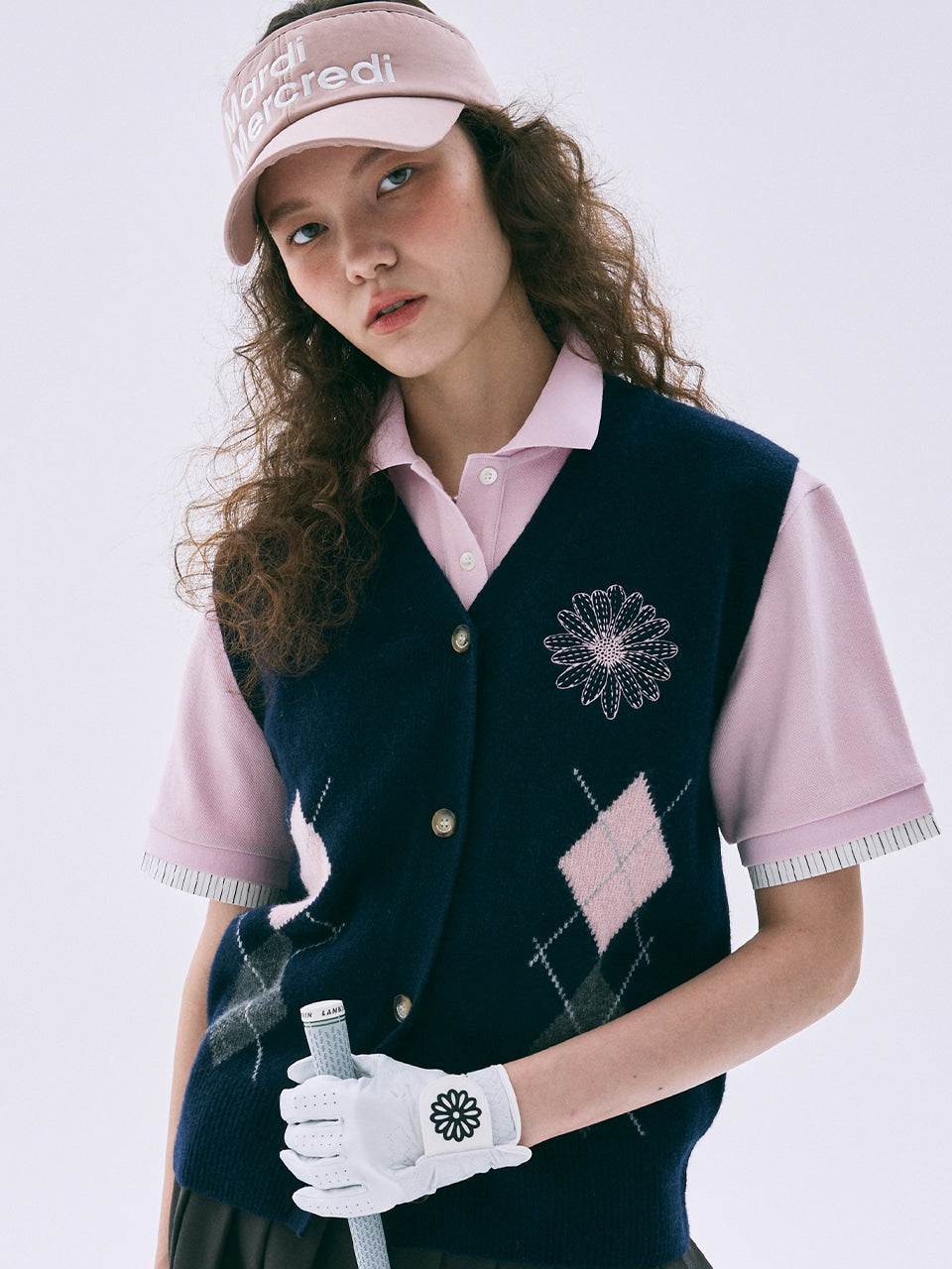Woman in golf attire with navy vest, pink shirt, and visor on a light gray background