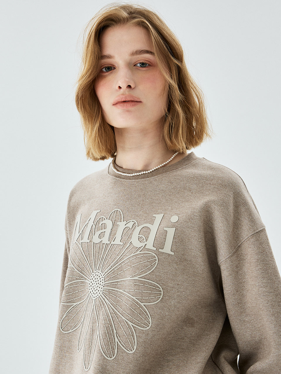 Person wearing a beige sweater with a floral design and text on a light gray background