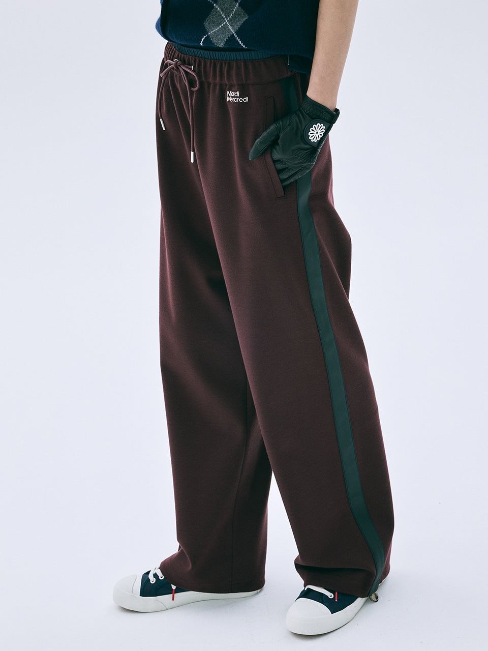 Brown track pants with green stripes worn by a person on a white background