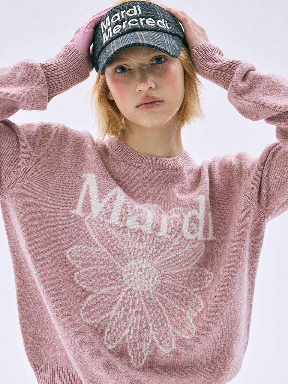 Person wearing a pink sweater with 'Mardi' text and a matching cap on a light background