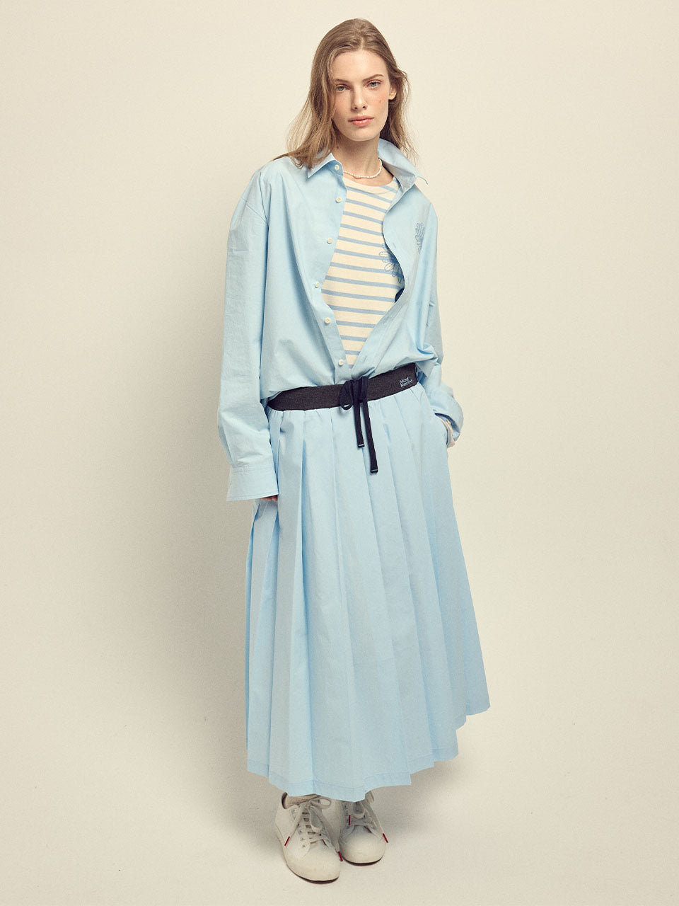 Woman wearing a light blue coat over a striped shirt on a beige background