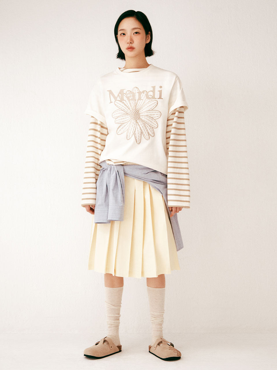 Person wearing a white sweater with 'Mardi' text and a yellow pleated skirt on a white background