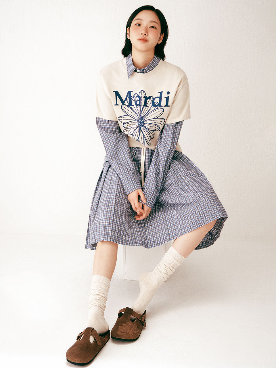 Person wearing a checkered dress over a sweater with 'Mardi' text on a white background