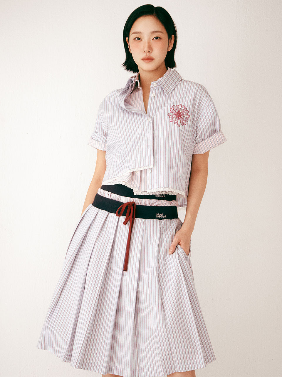 Woman wearing a white striped shirt and skirt with a black belt against a white background