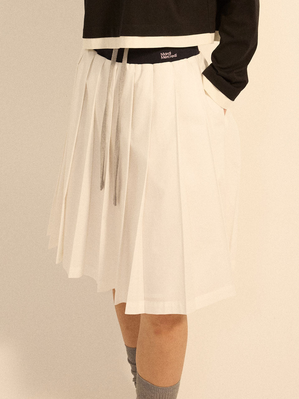 White pleated skirt worn by a person on a beige background