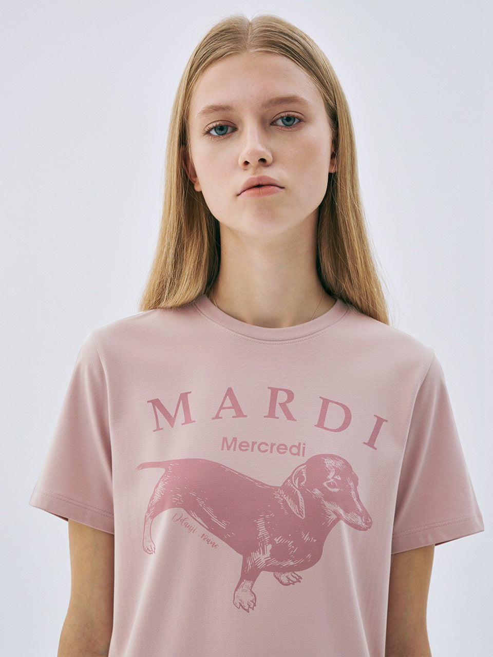 Person wearing a pink t-shirt with 'Mardi Mercredi' and a dachshund graphic on a white background