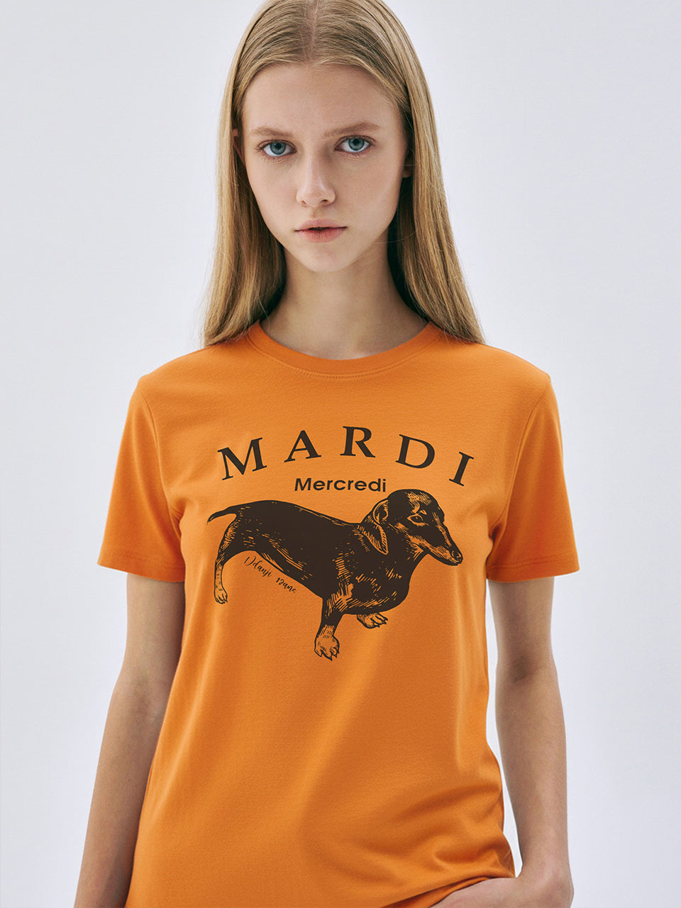 Person wearing an orange t-shirt with a dachshund graphic and 'Mardi Mercredi' text on a white background
