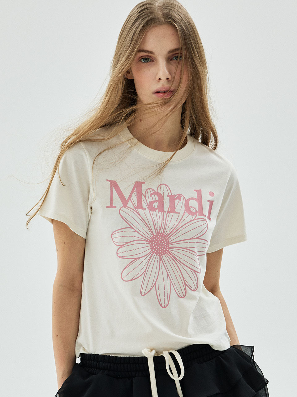 Woman wearing a white t-shirt with 'Mardi' and a pink flower design on a plain background