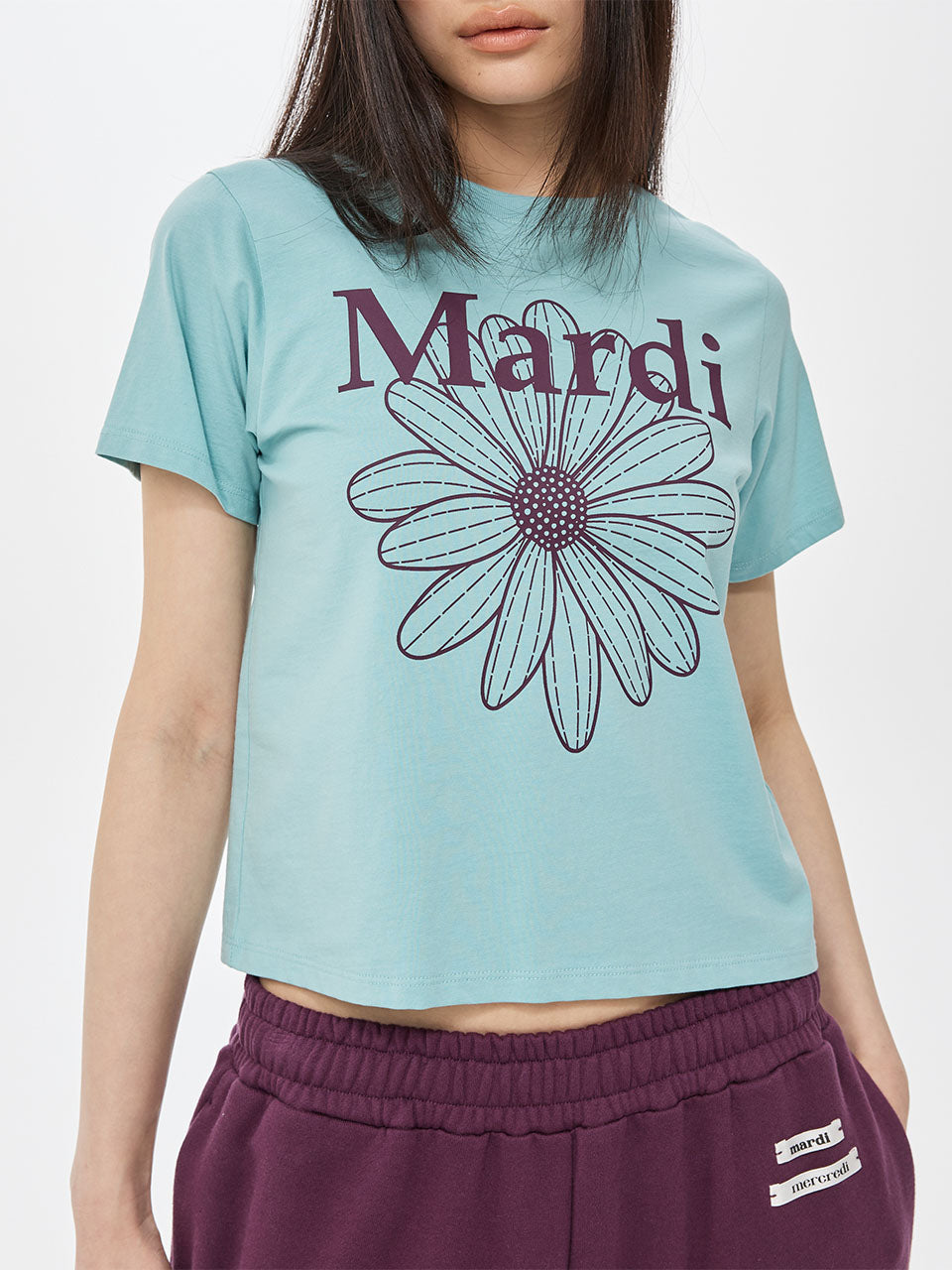 Person wearing a light blue t-shirt with a purple flower graphic and 'Mardi' text, paired with purple pants.