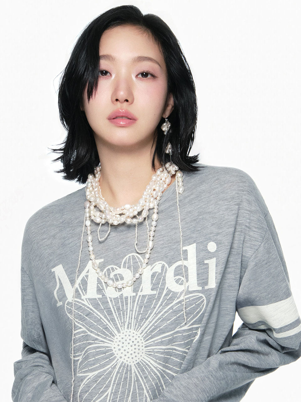 Person wearing a gray sweater with a brand logo and pearl necklace on a white background