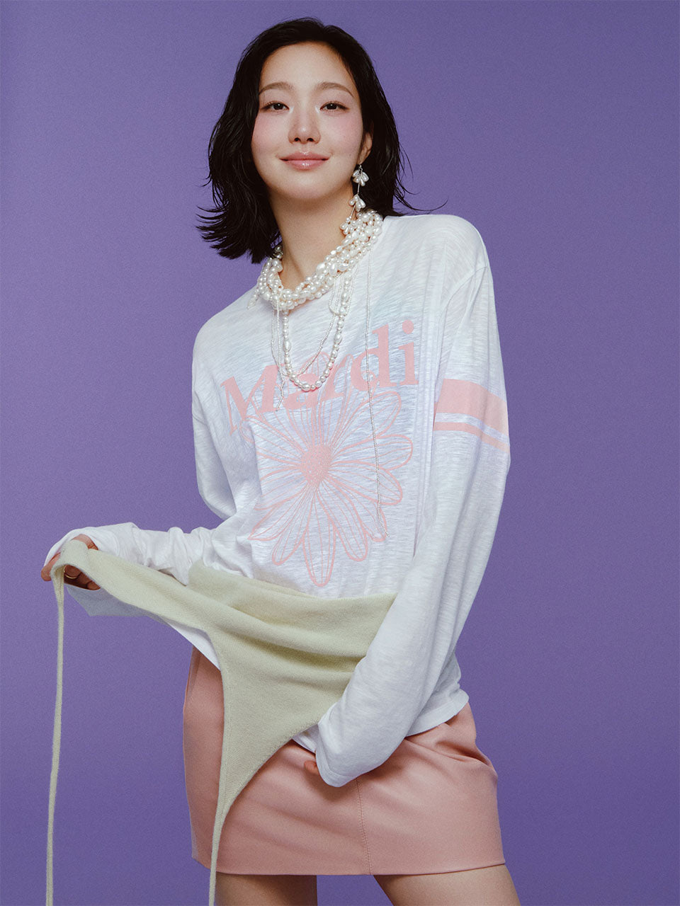Woman wearing a white sweater with 'Mardi' text and pink skirt on a purple background