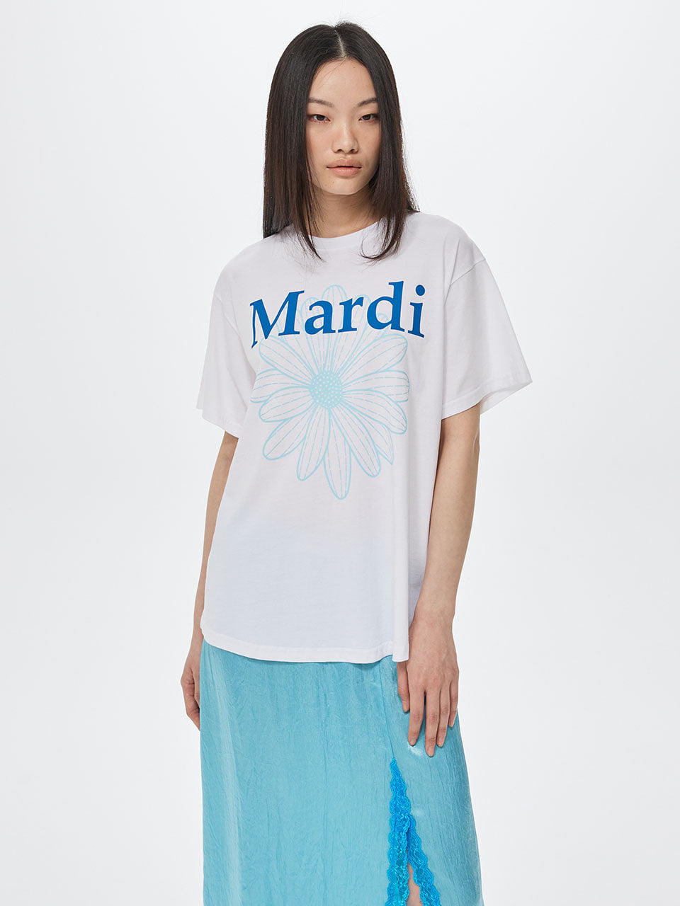 Woman wearing a white t-shirt with 'Mardi' and a blue flower design on a plain background