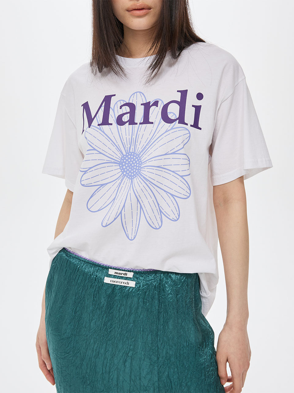 Person wearing a white t-shirt with a blue flower and 'Mardi' text on a plain background