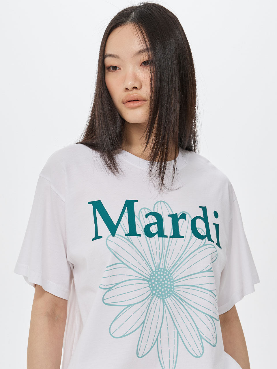 Person wearing a white t-shirt with 'Mardi' and a flower design on a plain background