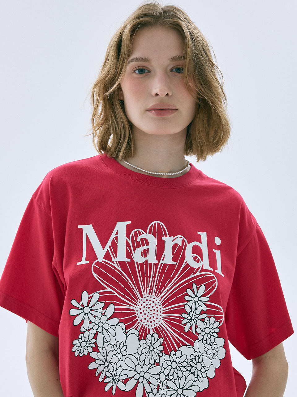 Person wearing a red t-shirt with white floral design and 'Mandi' text on a plain background