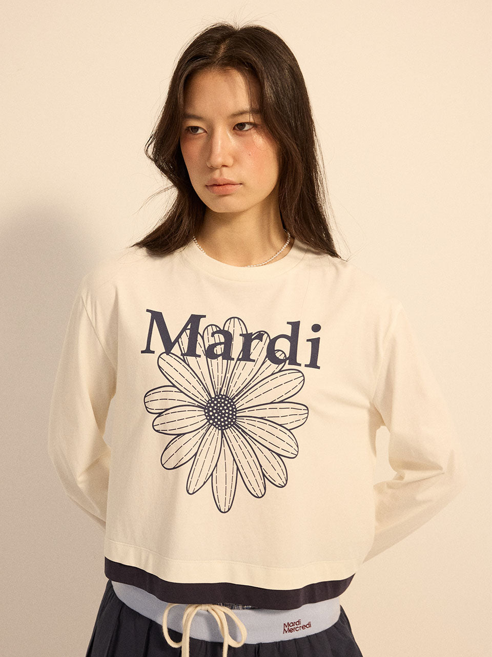 Woman wearing a white sweatshirt with a black flower design and 'Mardi' text on a beige background