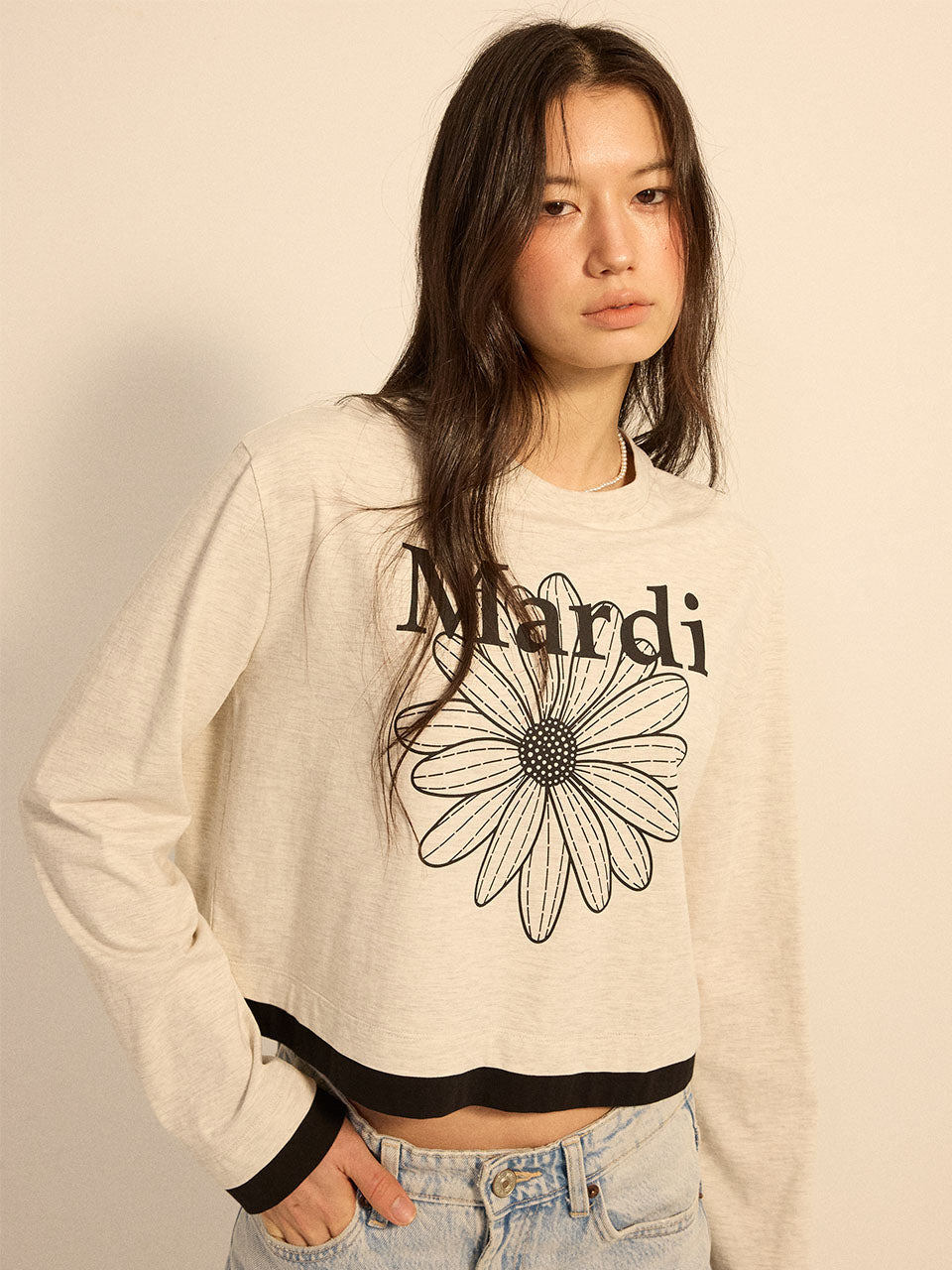 Person wearing a beige sweatshirt with a black flower design and 'Mardi' text on a plain background
