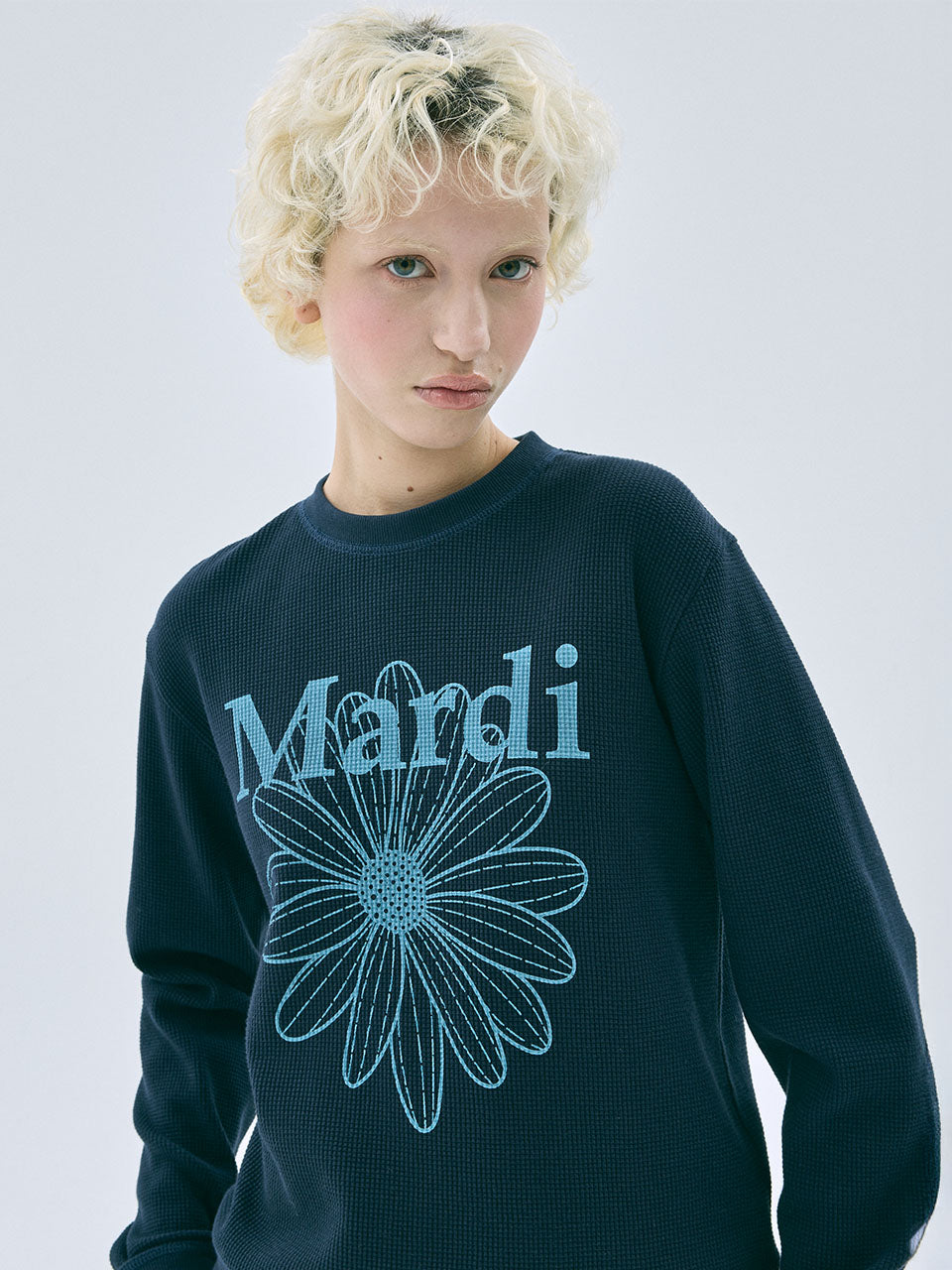 Person wearing a dark blue sweater with a floral design and 'Mandi' text on a light gray background