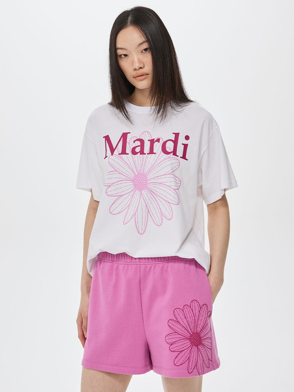 Person wearing a white t-shirt with 'Mardi' and pink shorts with floral designs on a white background